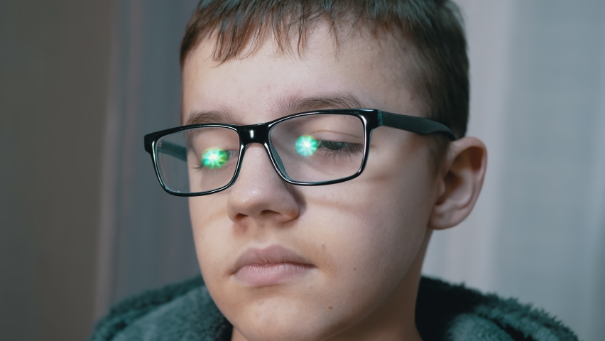 Tired Sad Child in Glasses with Downcast Eyes, Drooping Gaze Looks Down, Sighing. Face of thinking, offended, smart handsome boy with reflected highlights in glasses. Concept of education, learning.