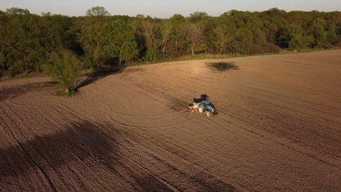Aerial view of blue tractor at work in autumn field. Preparation time of sowing. Shooting from drone flying over tractor in field with prepared soil for planting. Agriculture concept. Rural landscape.