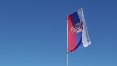 Serbian flag flapping on a pole with blue sky as background, copy space included
