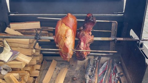 Ham rotating on spit in street grill. European street food. Big piece of pork cooking on a spit at street festival