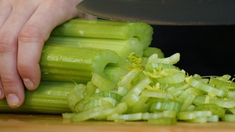 Women's hands with a knife cut celery on a wooden board