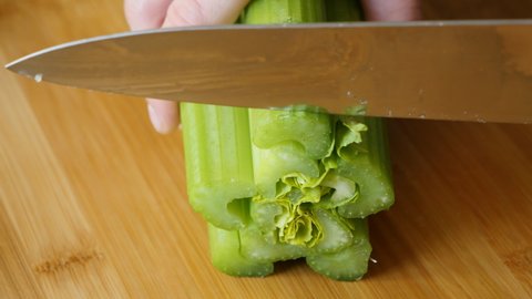 Women's hands with a knife cut celery on a wooden board