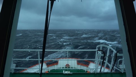 Vessel in storm. Bow breaks wave. Splashes of water. View from bridge. High waves. Strong pitching. White foam on water.