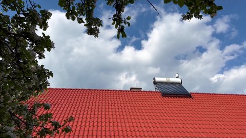 Miercurea Ciuc, Romania- 16 May 2022: Solar water heater boiler on rooftop, slow panoramic shot under the flowering apple trees.