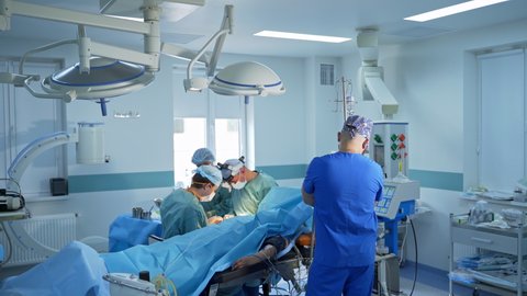 Two surgeons conducting neurosurgical operation. Anesthesiologist stands nearby watching the process.