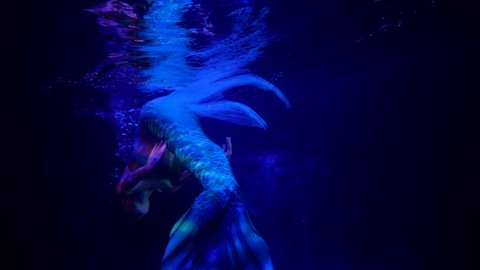 close-up of a mermaid's tail in blue water. the woman swims away. streaks of red light slide