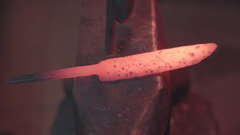 Blacksmith manually forging molten metal in smithy workshop. Damascus steel knife.