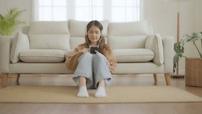 Happy young asian woman relaxing at home. Female smile sitting on sofa and holding mobile smartphone. Girl using video call to friend