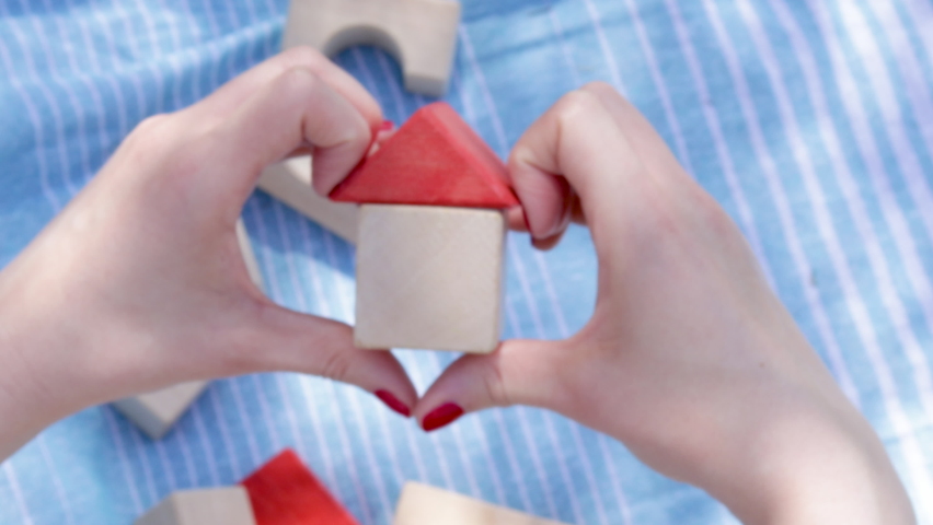 Defocused blurred 4k video.house from wooden cubes in woman's hand, red color nail, blue blanket and another eco toys in background. Mortgage property insurance, personal own home concept. copy space. | Shutterstock HD Video #1090353885