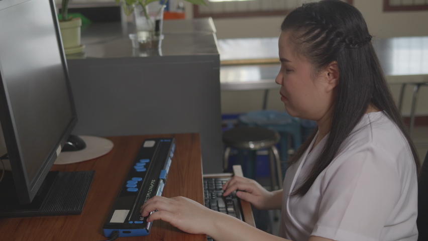 Asian woman with blindness disability using computer with refreshable braille display or braille terminal a technology assistive device for persons with visual impairment in workplace. Royalty-Free Stock Footage #1090353955