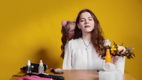 A little girl hairdresser does her hair on her client's head on a yellow background. Children as adults