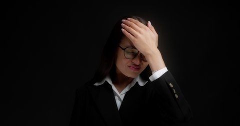 Business woman with long dark hair, glasses and office clothes forgot something, holds her forehead with her fist, bad memory. Isolated on a black background