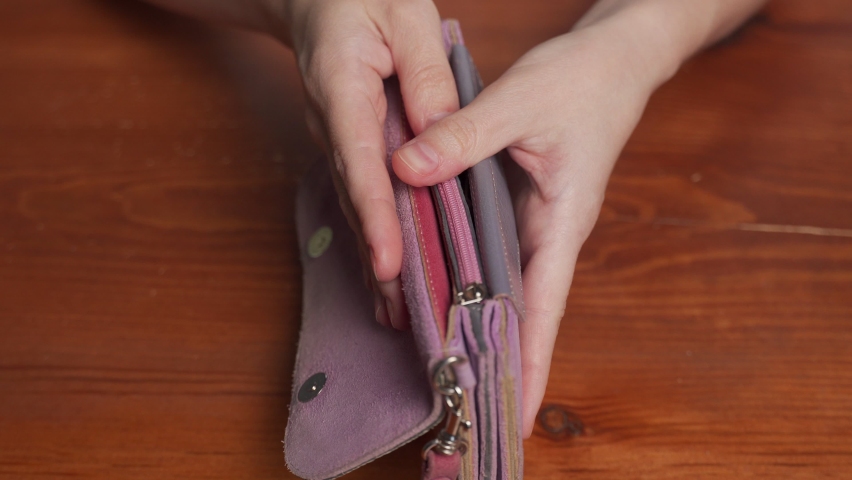 Poor woman looks for cash opening empty wallet against wooden table. Female hands hold purple purse with no money. Poverty concept close view Royalty-Free Stock Footage #1090356141