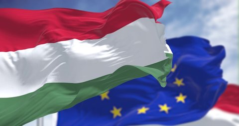 Seamless loop in slow motion of the national flag of Hungary waving  with blurred european union flag in the background on a clear day. Democracy and politics. European country. Selective focus.