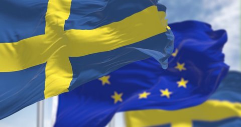 Seamless loop in slow motion of the national flag of Sweden waving with blurred european union flag in the background on a clear day. Democracy and politics. European country. Selective focus.