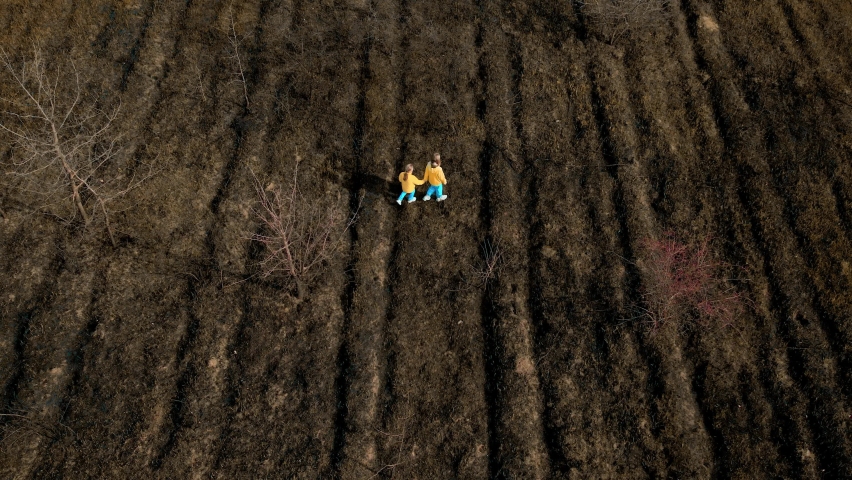 Ukrainian girls in clothes in the colors of the Ukrainian flag on the ground, destroyed and burned. Crisis, peace, stop the aggression. Ukrainian national colors, Sad refugee children.