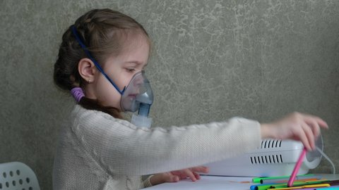 Child is sick and breathes through an inhaler in home. Little girl makes an inhalation vapor and draws a drawing.