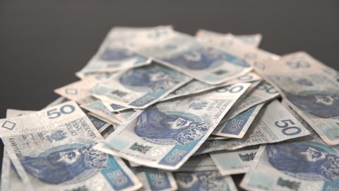 Bundles of packed Polish fifty-zloty bills fall on the loose bills lying around.