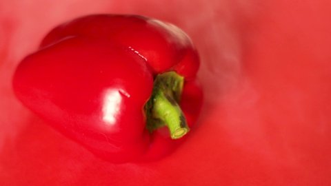 red bell pepper lies on a red background, there is smoke around it