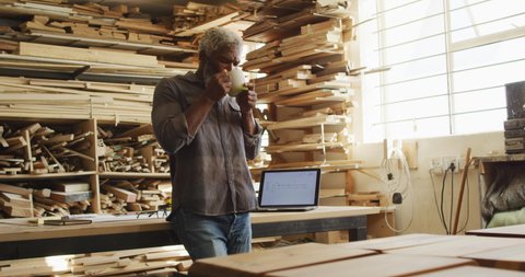African american male carpenter drinking coffee in a carpentry shop. carpentry, craftsmanship and handwork concept