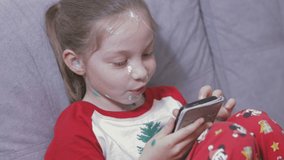 a little girl with chickenpox is sitting on the couch and playing online games on her phone