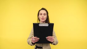 Surprised woman with a tablet with papers in her hands stands on a yellow background, reads with a shocked face and moves her head to the side showing a NO sign.