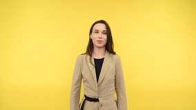 Joyful beautiful woman in a suit shows a heart gesture and smiles on a yellow background. Positive business woman showing love gesture in camera isolated.