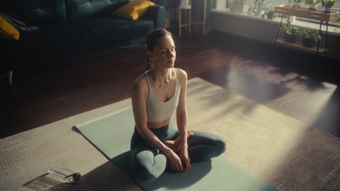 Portrait of a Happy Fit Young Woman Meditating During Morning Workout on Yoga Mat at Home in Sunny Apartment. Healthy Lifestyle, Fitness, Wellbeing and Mindfulness.