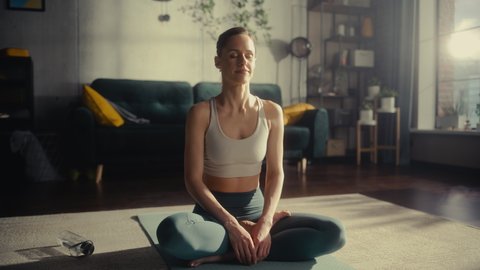 Athletic Young Female Exercising, Practising Meditation in the Morning in Her Bright Sunny Room at Home. Beautiful Woman in Sports Clothes Practising Mindfulness on Yoga Mat.