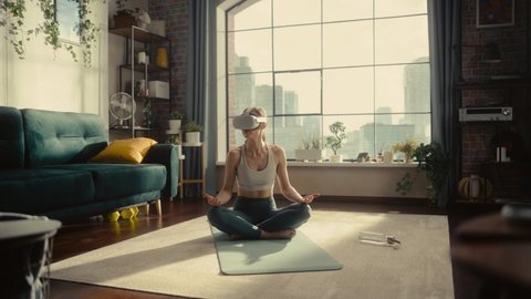 Young Athletic Woman Wearing Virtual Reality Headset, Practising Meditation in Modern Futuristic Way in Bright Sunny Home Living Room. Healthy Lifestyle, Fitness, Wellbeing and Mindfulness Concept.