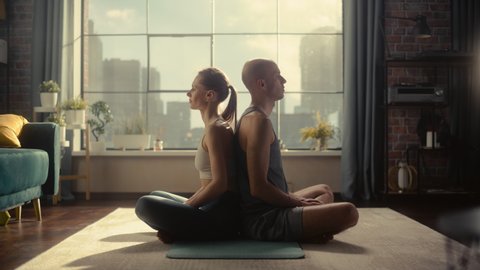 Young Beautiful Couple Exercising, Practising Meditation in the Morning in Bright Sunny Loft Apartment. Healthy Lifestyle, Fitness, Wellbeing and Mindfulness Concept.
