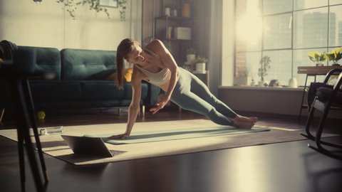 Young Beautiful Female Exercising, Stretching and Practising Yoga with Trainer via Video Call Conference in Bright Sunny Loft Apartment. Healthy Lifestyle, Fitness, Wellbeing and Mindfulness Concept.