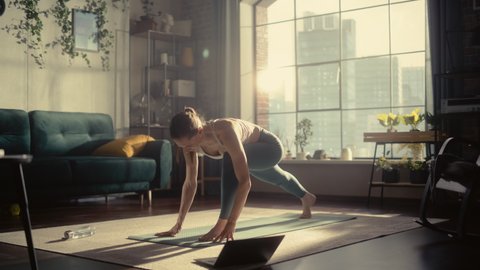 Young Athletic Woman Exercising, Stretching and Practising Yoga in the Morning in Bright Sunny Home Living Room. Online Fitness training Workout via Laptop Computer.