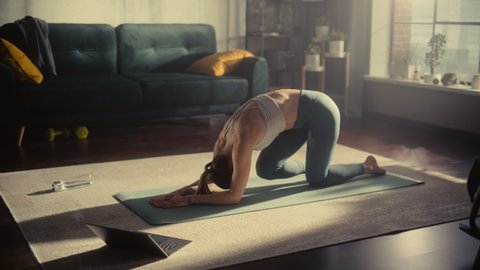 Athletic Young Female Exercising, Stretching and Doing Yoga while Watching Training Video on Laptop Computer. Beautiful Woman in Sports Clothes Practising Different Asana Poses on the Mat.
