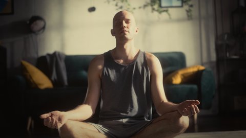 Athletic Young Man Exercising, Practising Meditation in the Morning in His Bright Sunny Room at Home. Handsome Bald Male in Sports Clothes Practising Mindfulness on Yoga Mat.