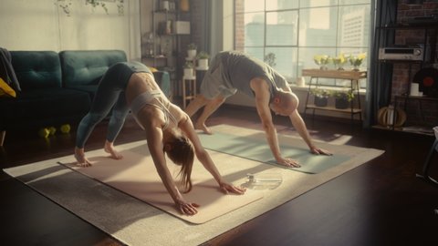 Athletic Young Couple Exercising Together, Stretching and Doing Yoga in the Morning in Bright Sunny Room at Home. Beautiful Man and Woman in Sports Clothes Practising Different Asana Poses on the Mat.