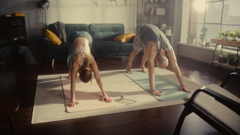 Portrait of a Happy Fit Young Couple Doing Stretching and Core Strengthening Yoga Exercises During Morning Workout at Home in Sunny Apartment. Healthy Lifestyle, Fitness, Wellbeing and Mindfulness.