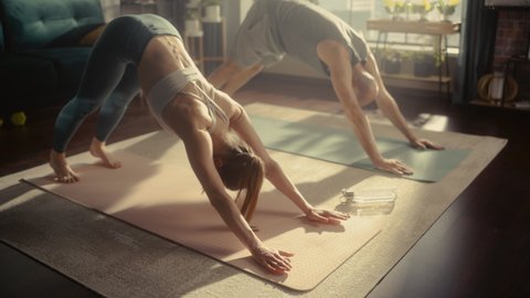 Young Athletic Couple Exercising, Stretching and Practising Yoga in the Morning in Bright Sunny Home Living Room. Healthy Lifestyle, Fitness, Wellbeing and Mindfulness Concept.
