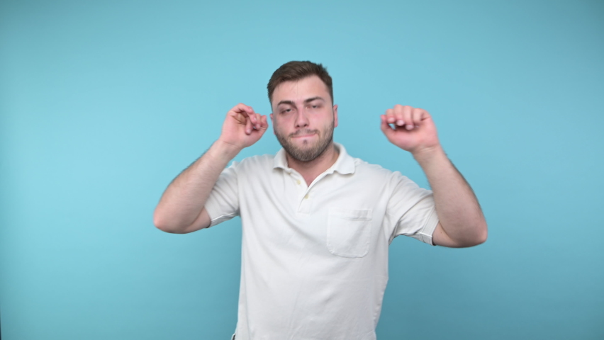 Joyful man with bristles and in a white T-shirt dances with happiness on a blue background and smiles.