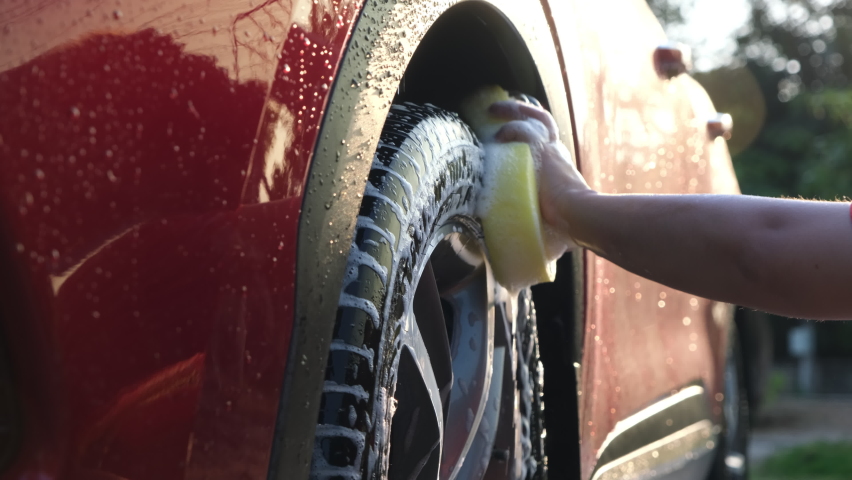 Close-up of a woman's hand washing the alloy wheels of a car with sponge and soap on the car wash. Manual car wash with white soap. Car wash service concept. | Shutterstock HD Video #1090365813