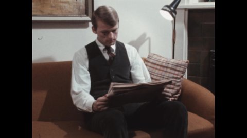1960s: clapperboard clap in living room set. Sofa in living room. Man sits on sofa with newspaper. Man reads paper at home. Secretarial positions available.