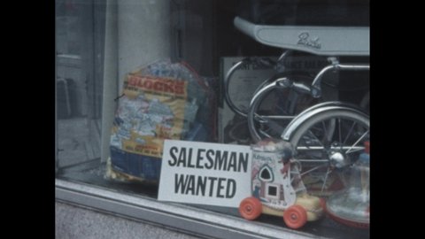 1960s: shop window sign for salesman wanted. Clapperboard outside shop window. Pram in window. Boss talks with employees. Men in shirts and ties at work.