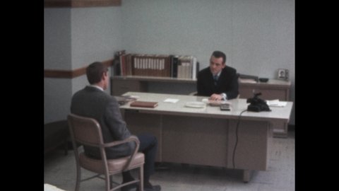 1960s: clapperboard in front of camera. Man sits at desk in interview. Man attends work search interview. Men shakes hands across desk. Men leave desk together
