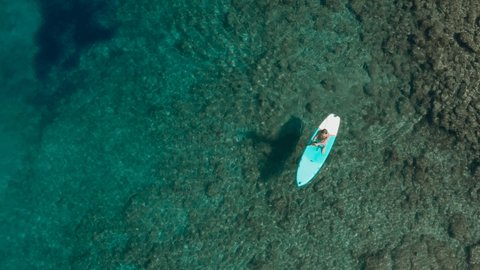 Directly above drone shot: Man paddling on a stand up board on turquoise water. People on vacation in Croatia enjoying water sport 