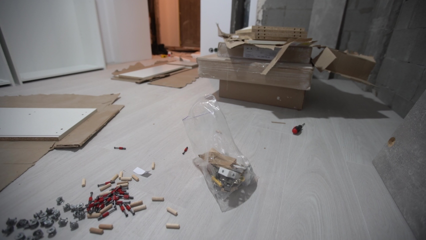 Parts of unfinished furniture, metal screws and tools lying on the floor with instruction manual for furniture assembly in the background. Moving to new home. | Shutterstock HD Video #1090367395