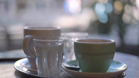 Cup of tea, coffee and glass of cold water on a table in cafe. White cups of fresh steaming americano and cup of tea on a table in cafeteria at morning with blurred background. High quality 4k video