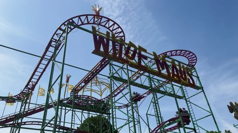 BERLIN, GERMANY - MAY 15, 2022: Small Rollercoaster Ride WILDE MAUS at Fun Fair, Carnival Neukoellner Maientage in the public park Hasenheide with a blue sky. With sound.