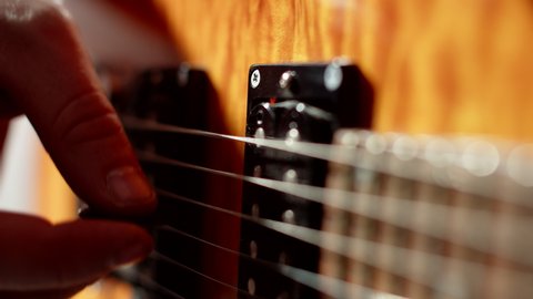 Closeup musicians fingers holding pick and playing strings of an electric guitar. Musician plays electric guitar with help of mediator