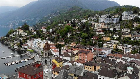Aerial flyover around the belfry tower of the Chiesa dei Santi Pietro e Paolo church and over the rooftops Ascona, Switzerland revealing the waters of Lago Maggiore and Alps in the background