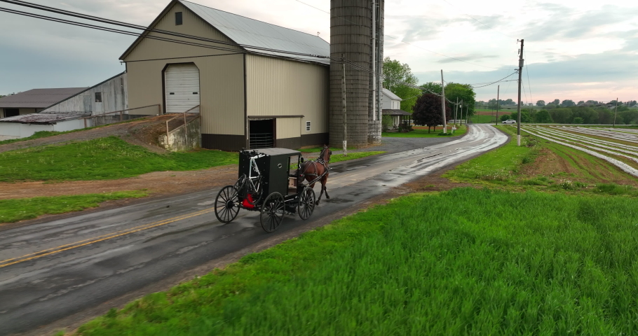 Aerial tracking shot of Amish horse and buggy passing farm. Amish family returns home after church on Sunday. Rural America in spring.